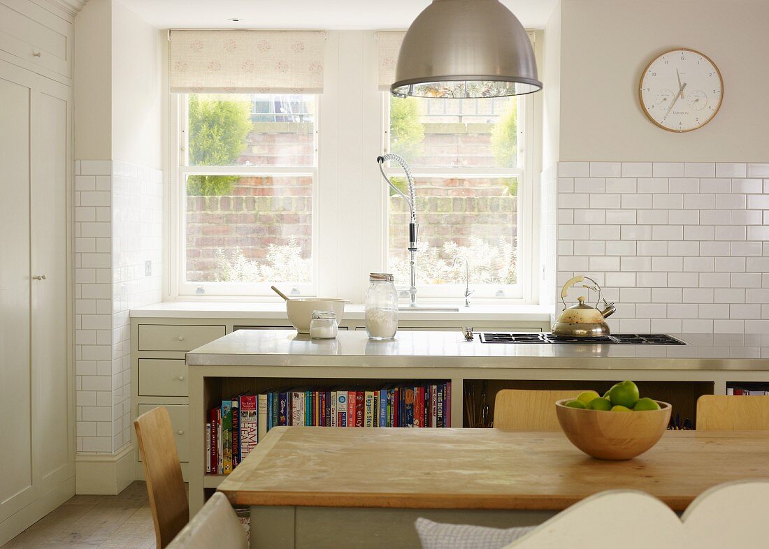 Landhaus Charme - Schlichter Esstisch vor Kücheninsel mit Kochfeld und Küchenzeile am Fenster