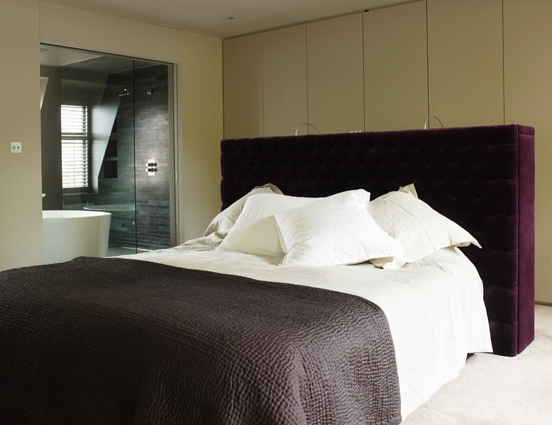 Doppelbett mit gepolstertem Kopfteil und violettem Bezug vor Wandschrank in modernem Schlafzimmer mit Bad ensuite