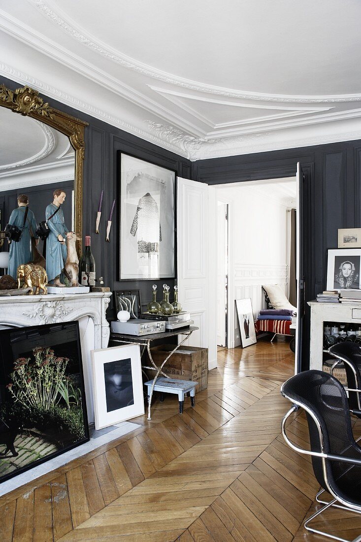 Diverse art works on a mantelpiece in front of a gold framed mirror in a drawing room with dark gray walls