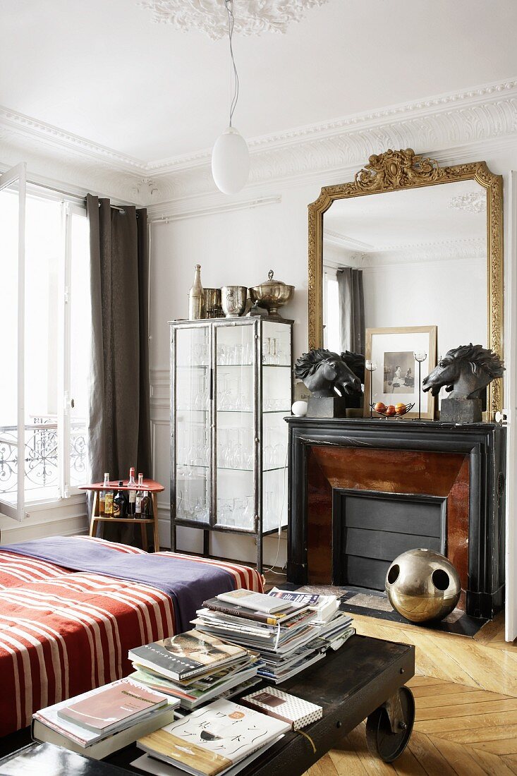 Schlafzimmer mit antikem Couchtisch auf Rollen neben dem Bett, Kamin und Goldrahmen-Spiegel
