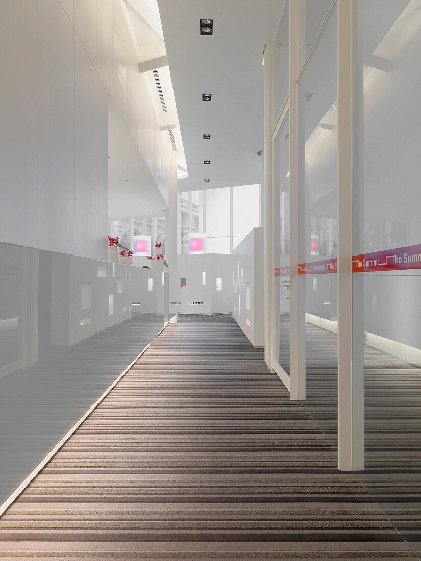Ein modern gestalteter Flur in einem öffentlichen Gebäude mit Milchglaswänden, abgehängter Decke und gestreiftem Teppichboden