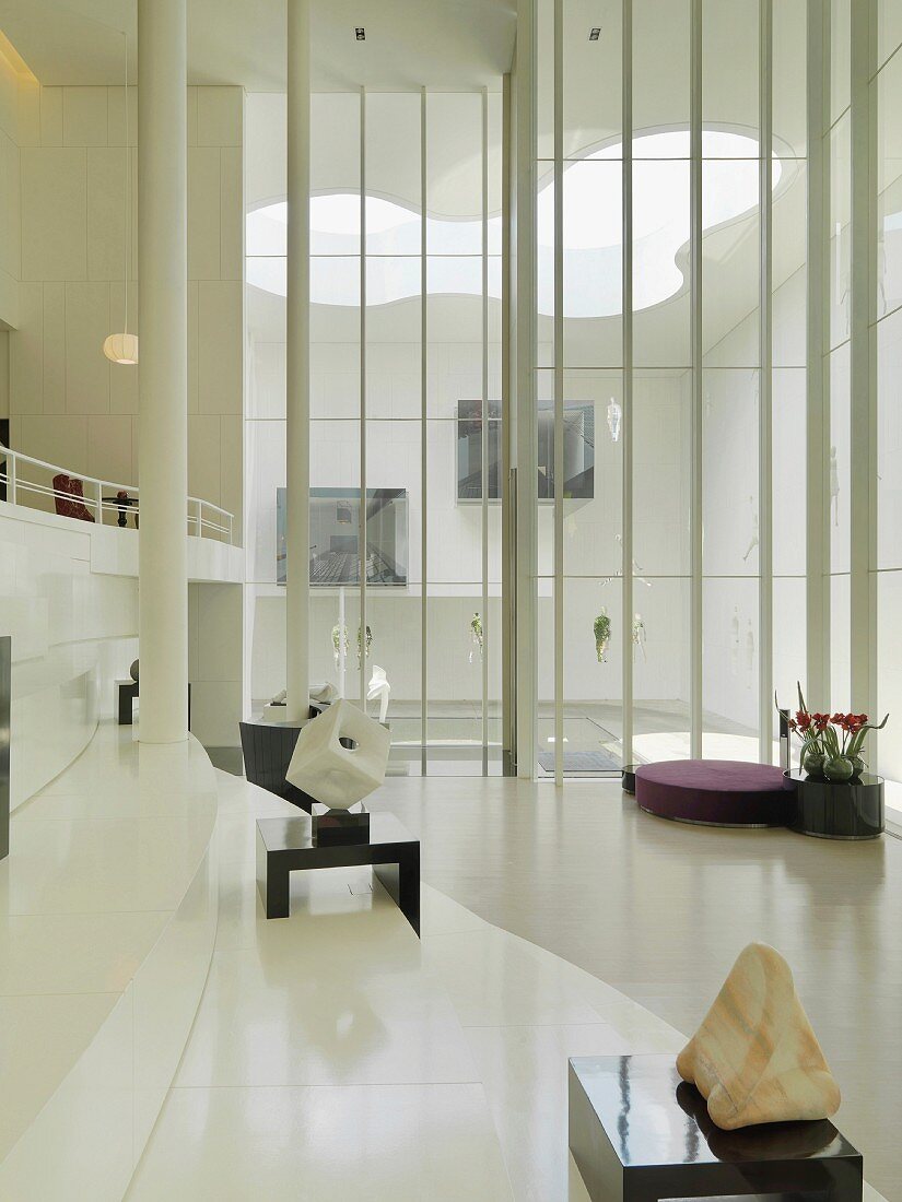 Zeitgenössische Skulpturen in einer Lobby mit Blick durch raumhohe Fenster auf den modern gestalteten Innenhof