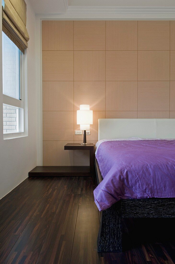 Ein gerastertes Holzpaneel ziert eine Wand des Schlafzimmers mit dunklem Holzboden