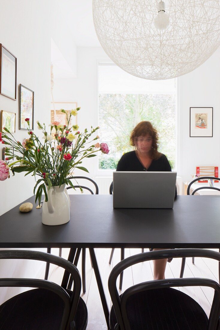 Woman working on dining table - designer pendant lamp above vase of flowers on black table