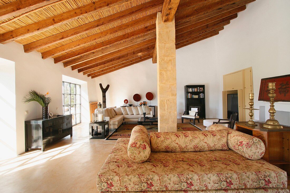 Romantische Nackenrollencouch im großen Wohnraum mit schräger Holzbalkendecke