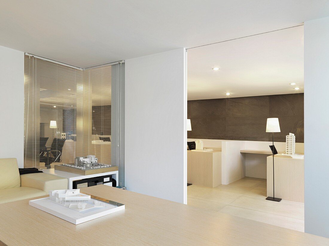Architekturmodell auf Holztisch in modernem Besprechungsraum und Blick durch offene Schiebetür ins Büro