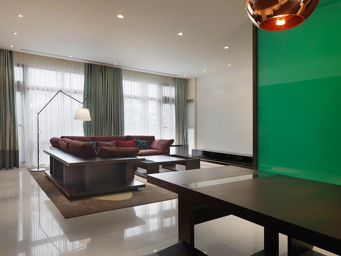Esstisch vor grünem Glaspaneel und freistehende Eckcouch in modernem Wohnraum