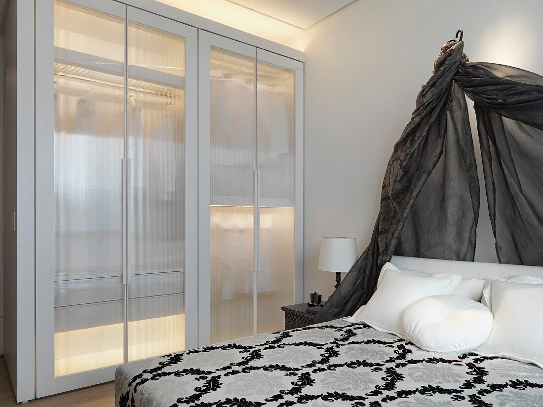 Bett mit Baldachin aus schwarzem transparenten Stoff neben beleuchteten Einbauschrank mit Glastüren