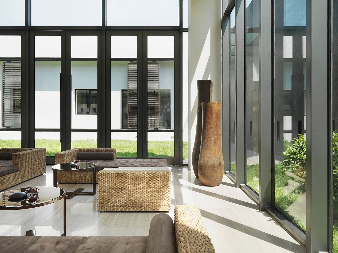 Sitzmöbel aus Rattan und hohe Bodenvasen vor Glasfront in modernem Aufenthaltsraum