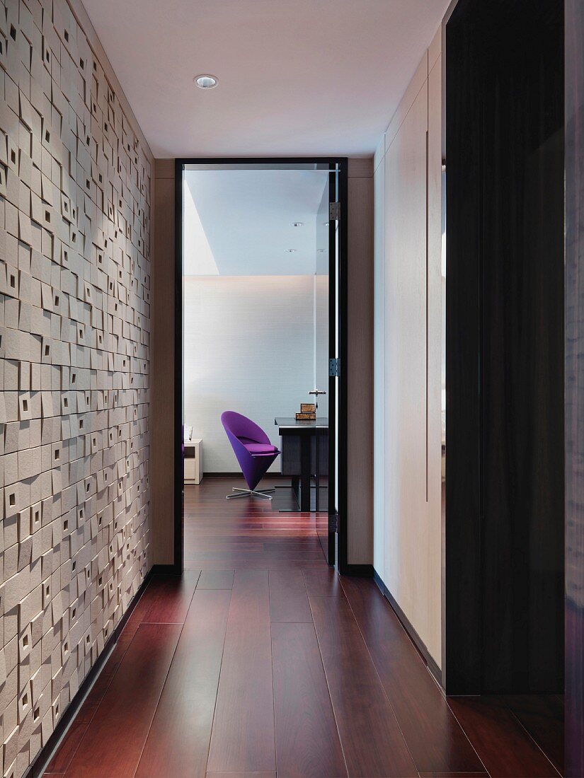 Gangflucht mit strukturierter Seitenwand und Blick durch offene Tür auf lilafarbenen Designerstuhl an einem Schreibtisch