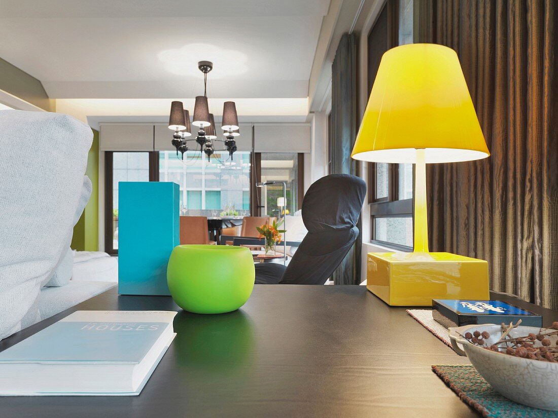 Farbige Lampe und Vasen im schlicht modernen Stil auf einem Schreibtisch und Hängelampe im Hintergrund