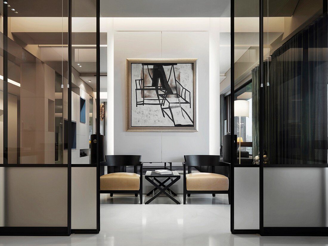 Blick durch getönte Glasschiebetüren auf modernes Gemälde über kleinem Sitzplatz mit schwarzen Holzmöbeln