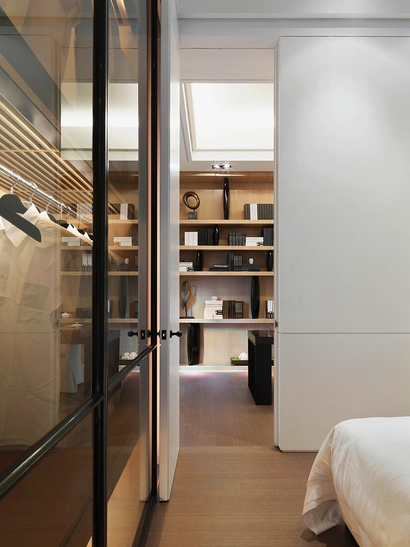 Blick vom Schlafzimmer vorbei an Kleiderschrank mit Glastüren auf Regal im asiatischen Stil mit eleganten Buchstützen