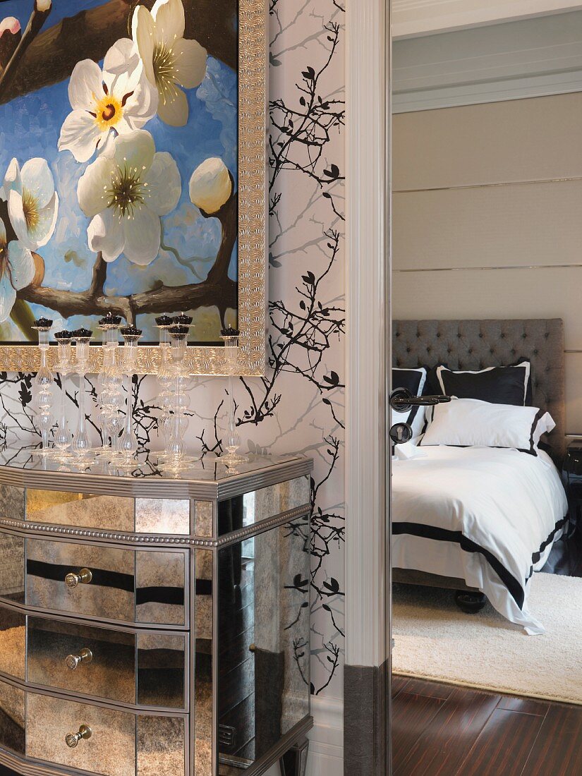 Spiegelkommode unter stilisiertem Kirschblütengemälde und Blick auf das schwarzweiss bezogene Doppelbett
