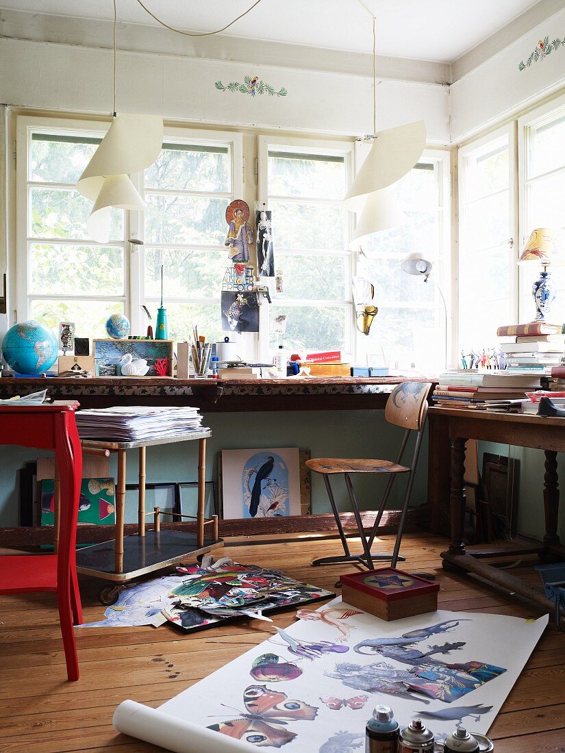 Painter's studio with laden tables below windows and roll of paper with realistic pictures of butterflies on floor