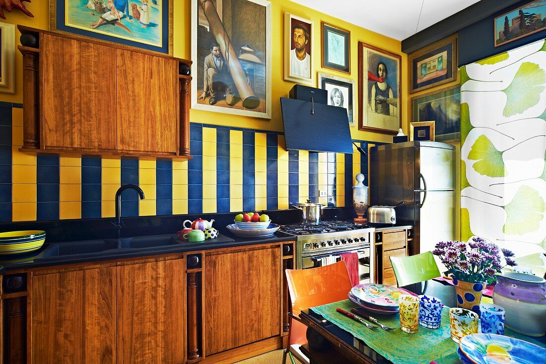 Moderne Holzküche mit großer Bildersammlung an den Wänden; im Vordergrund ein gedeckter Tisch mit farbenfrohem Keramikgeschirr