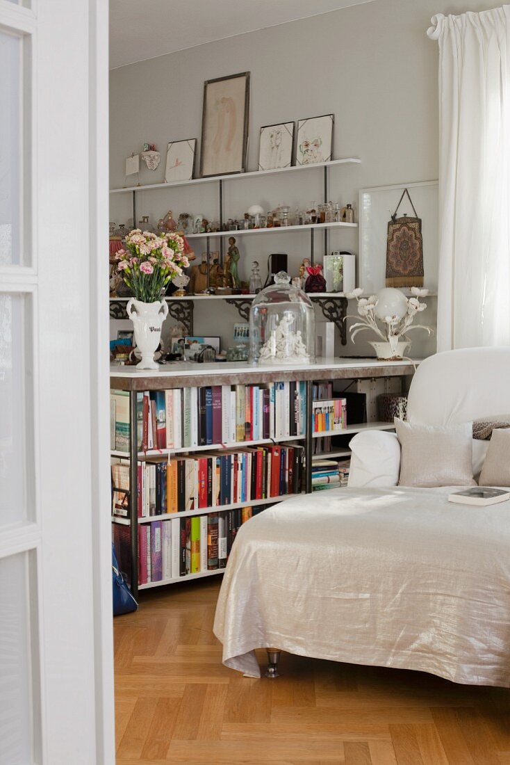Halbhohes Bücherregal als Raumteiler neben Recamiere mit weißem Bezug
