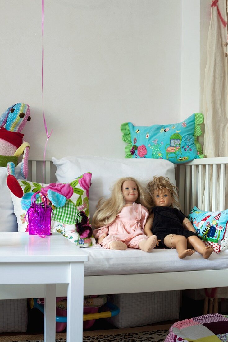 Puppen und bunte Kissen auf einem weissen Kinderbett