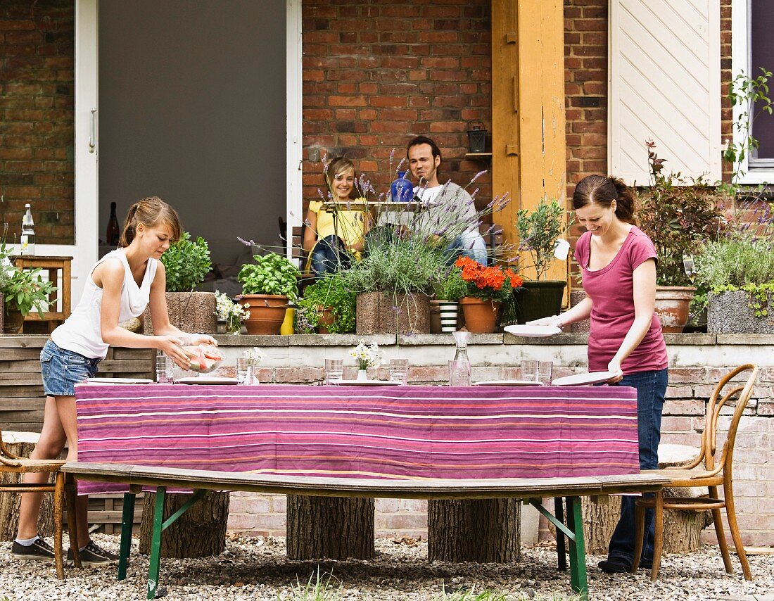 Mädchen und Frau decken den Gartentisch vor dem Haus