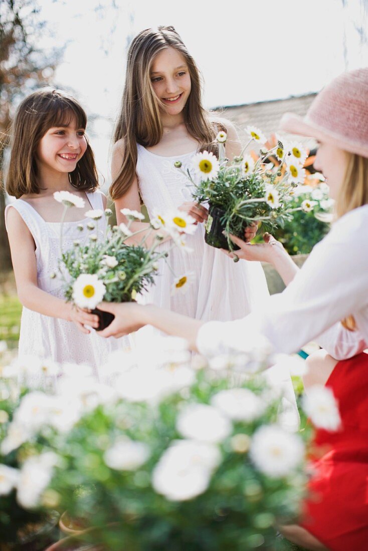 Frau überreicht zwei Mädchen Blumentöpfe mit Margeriten