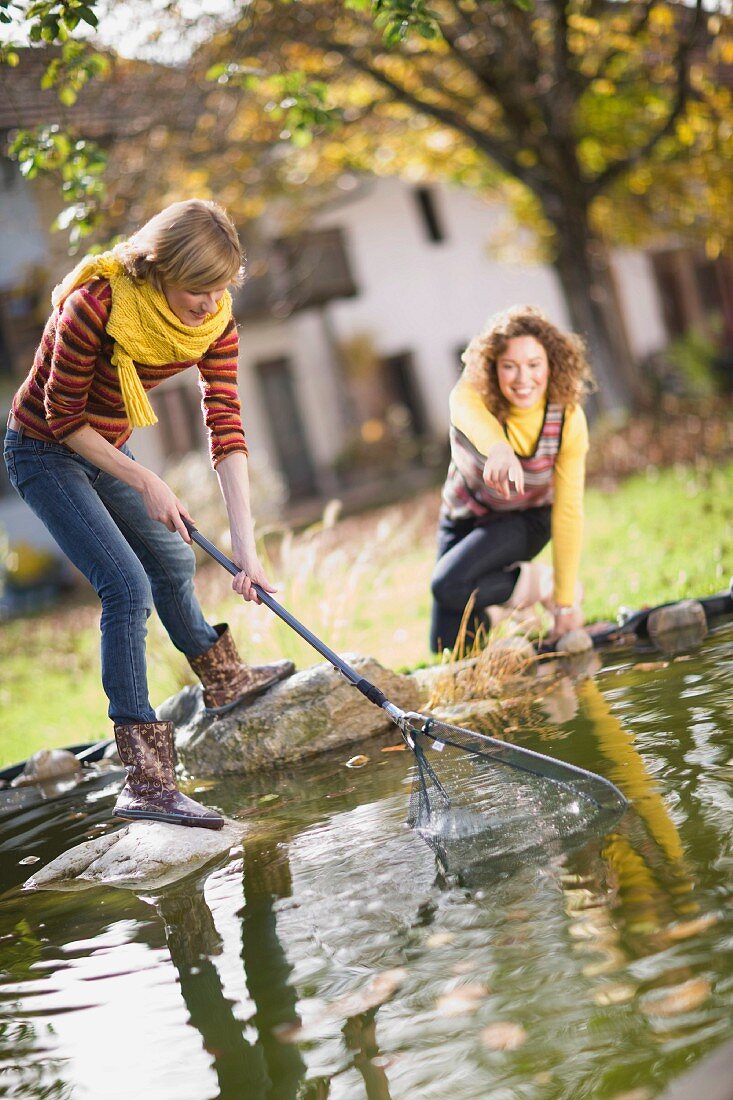 Zwei junge Frauen reinigen Gartenteich mit Rechen