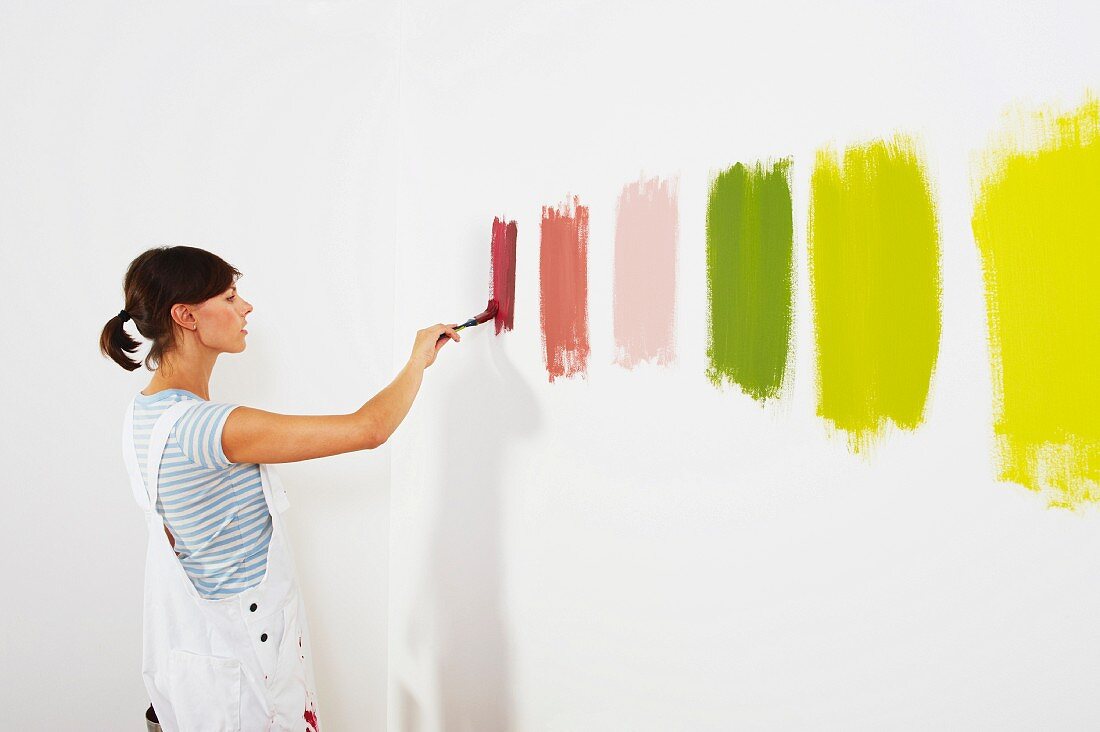 Junge Frau malt Farbteststreifen an Zimmerwand