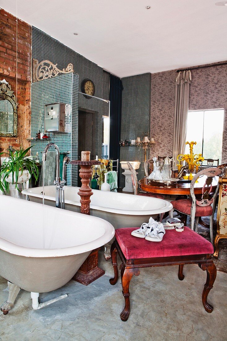 Twin freestanding bathtubs with standpipe tap fittings and various antique furnishings in crammed lounge-style bathroom