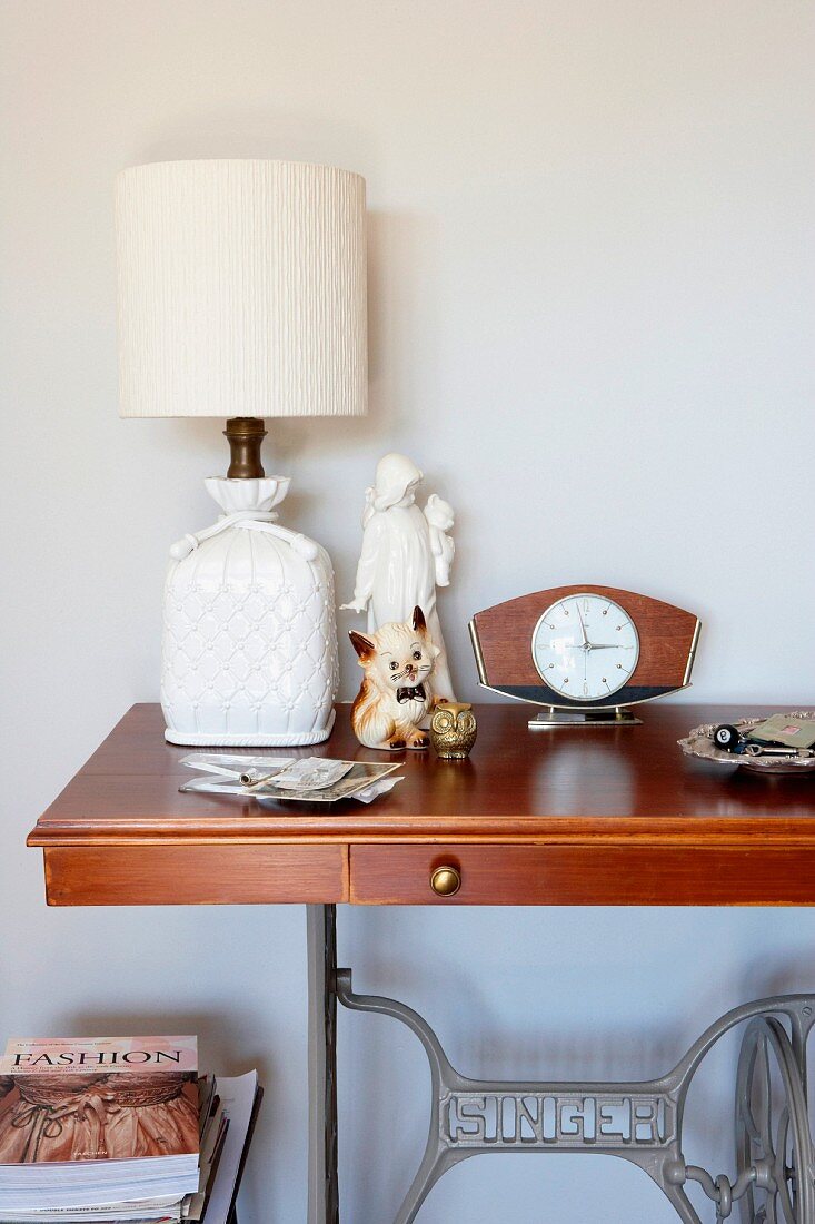 Table lamp with white lampshade on former sewing machine table against white wall
