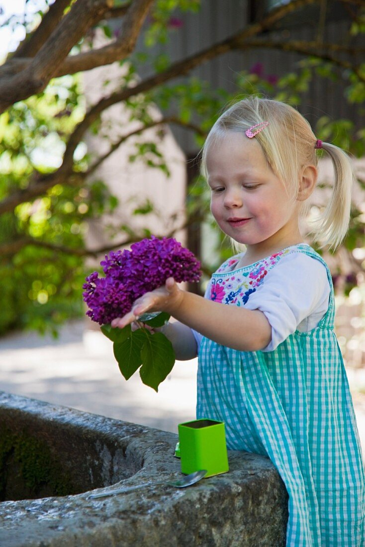 Kleines Mädchen hält Blumen am Brunnen