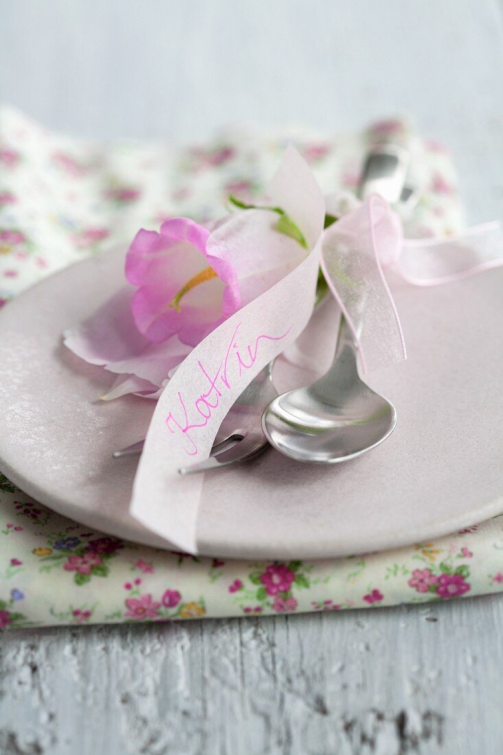 Besteck mit Glockenblume und Namenszug auf rosa Teller
