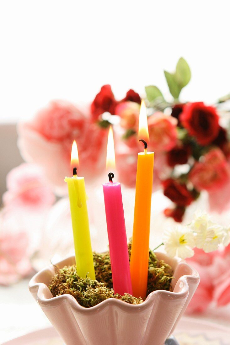 Lit candles in front of bouquet of roses