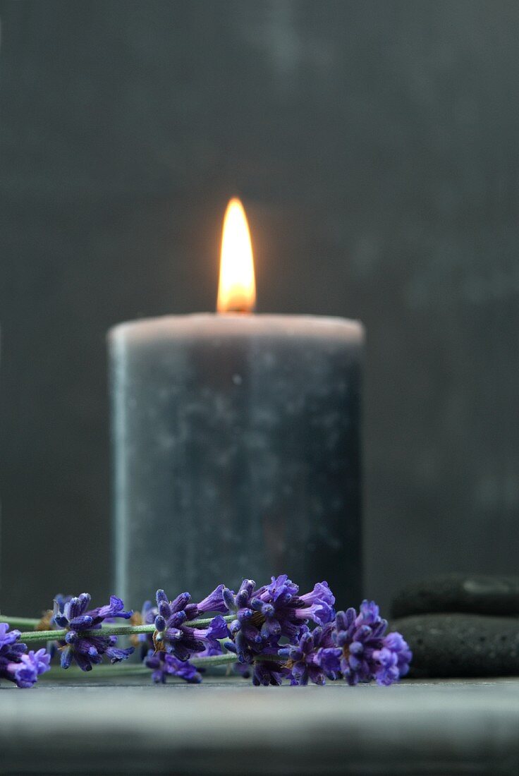 Brennende Kerze zwischen getrockneten Lavendelblüten und flachen Steinen