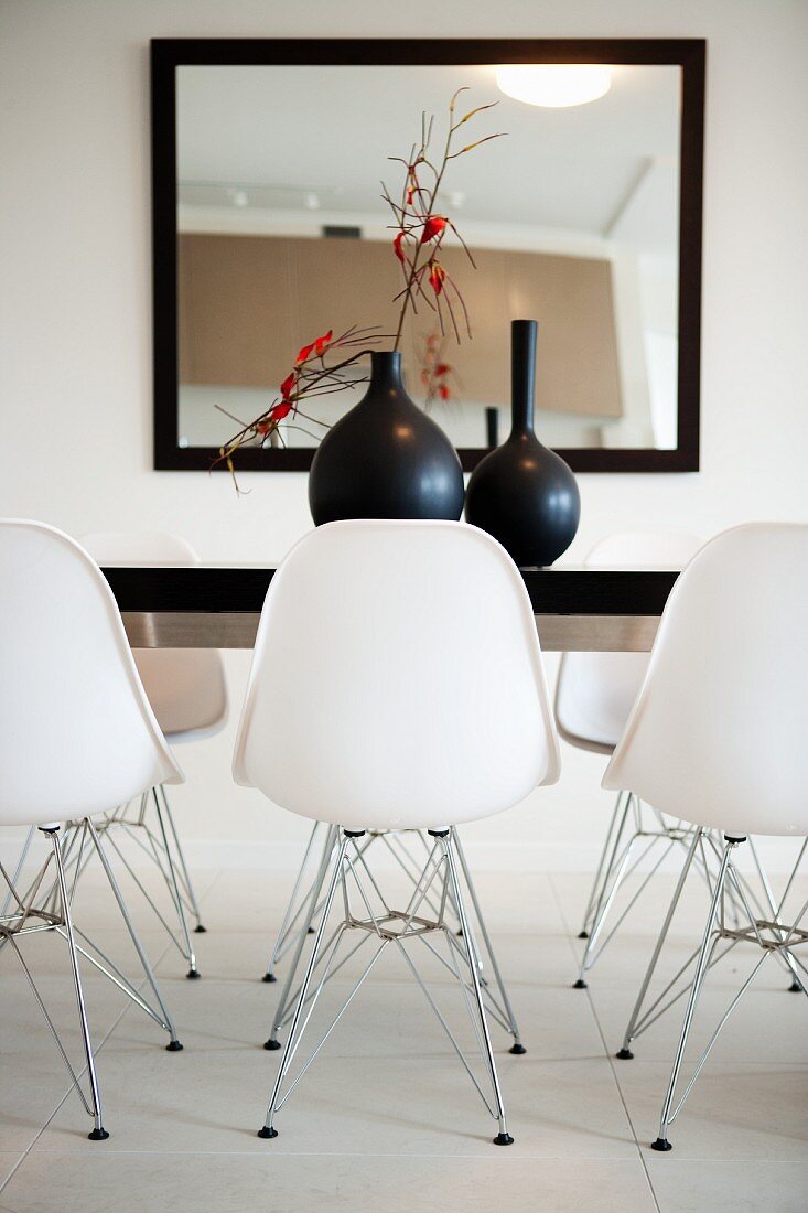 Ausschnitt eines Esszimmers mit großem, gerahmten Wandspiegel, schwarzem Tisch und weissen Designer-Schalenstühlen