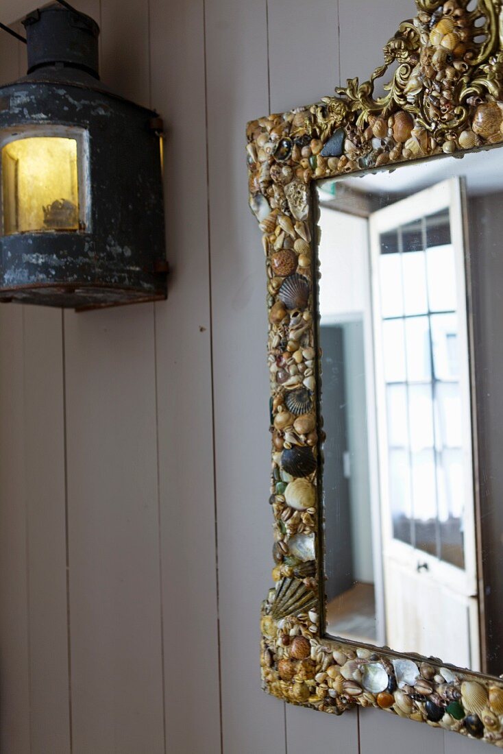 Wall mirror with a shell frame and antique wall lantern on a wood paneled wall