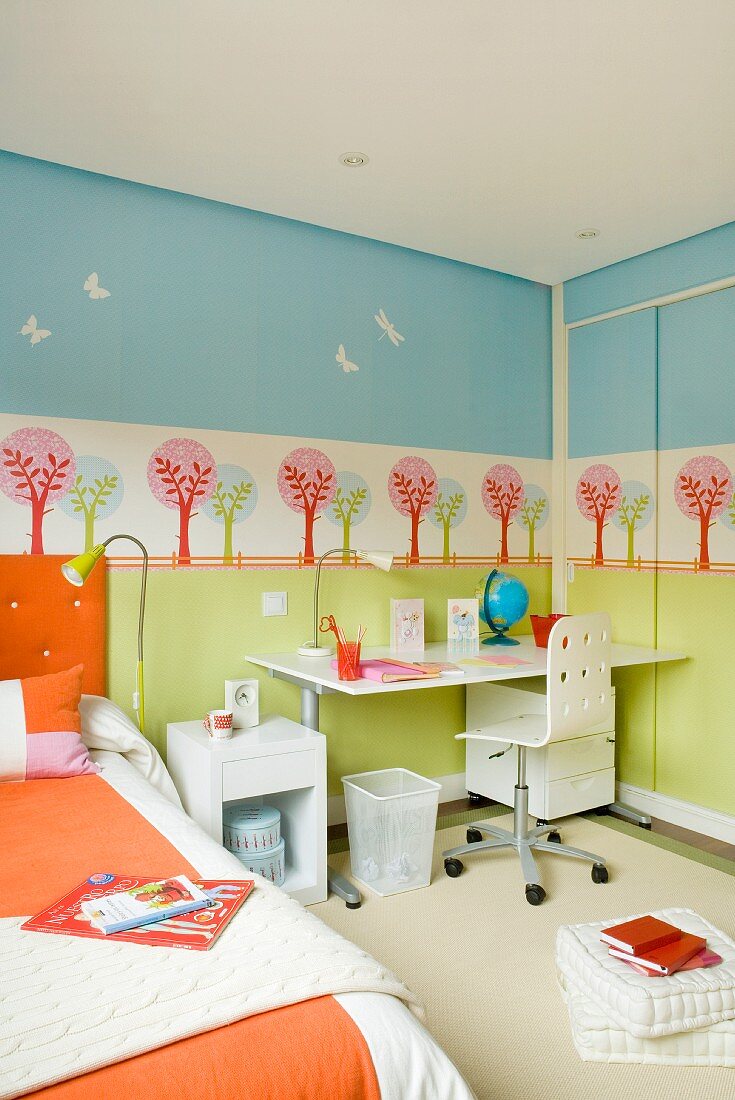 Pastellfarben im Kinderzimmer - in Schablonentechnik bemalte Wand hinter neutral weißem Schreibplatz und orangefarben bezogenem Bett