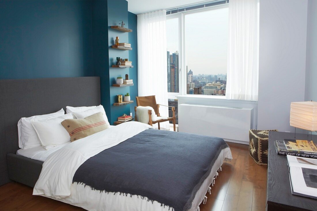 Urbanes Schlafzimmer mit grauem Doppelbett vor azurblauer Wand