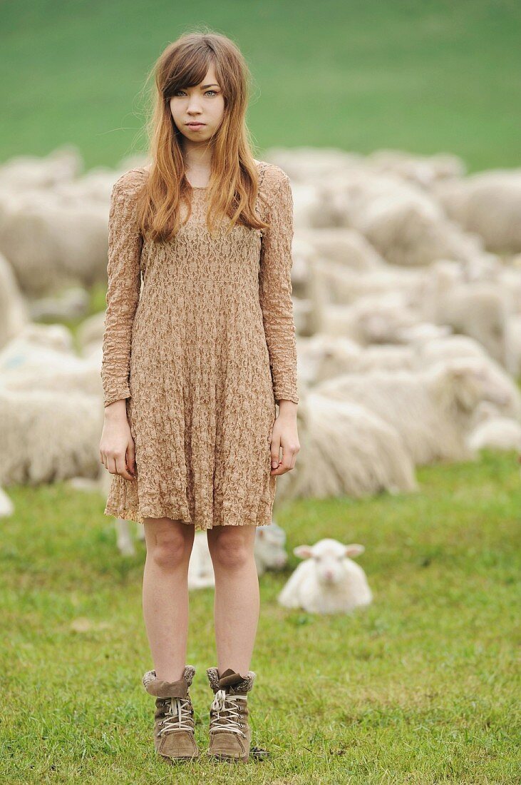 Junges Mädchen steht auf Wiese vor Schafherde