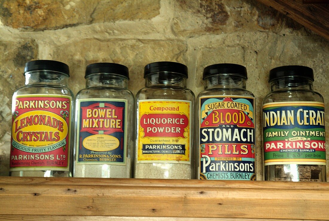 Screw-top glass jars with vintage, English labels on wooden shelf against stone wall