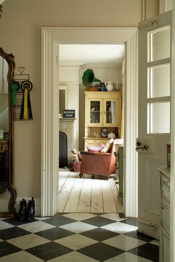 Blick durch geöffnete Eingangstür in den Flurbereich und in gemütlichen Wohnraum mit weißem Dielenboden im Vintagestil
