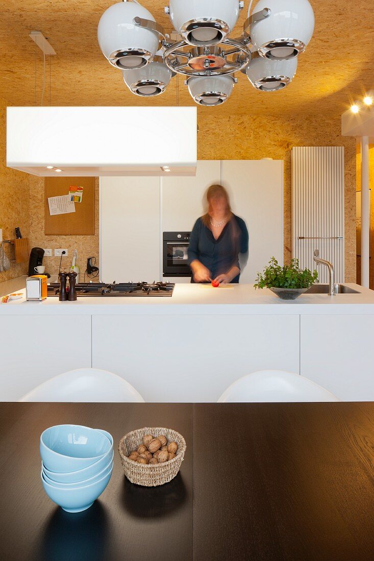 View across dining table of woman at modern kitchen counter in open-plan kitchen