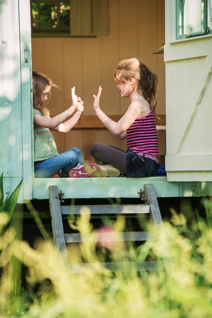 Two girls sitting and playing in the entrance to a small summer house