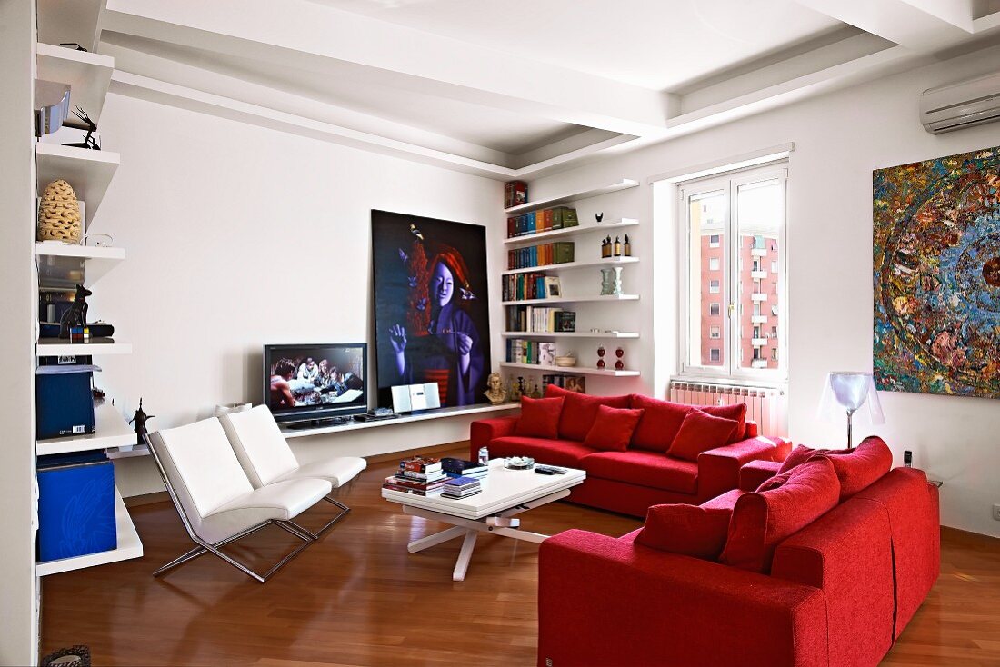 Modern seating area with two comfortable, red sofas and white upholstered armchairs around modern coffee table