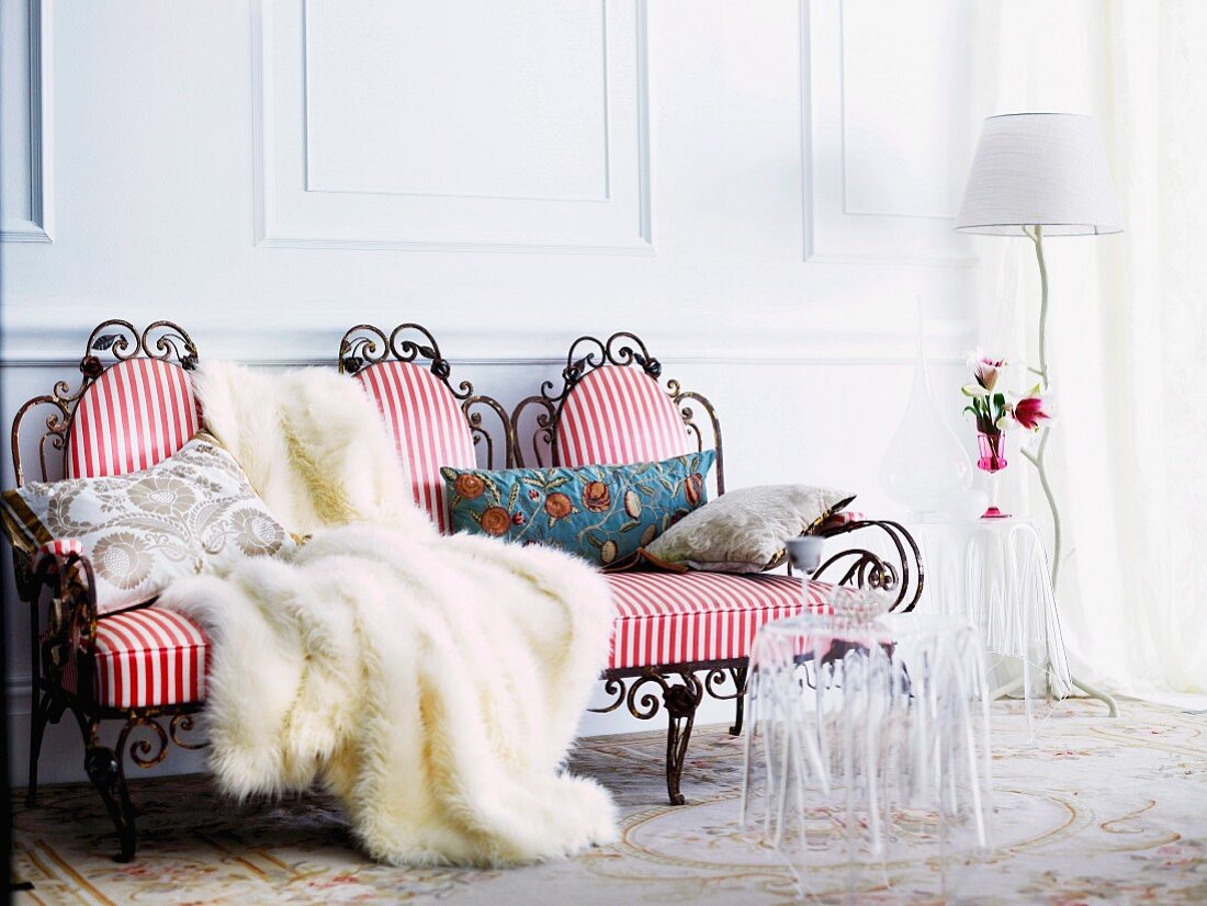 Romantic seating area with draped fur blanket on red and white striped upholstery of delicate, antique-style wire bench