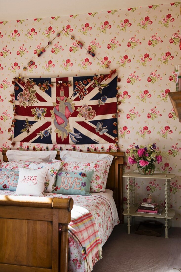 Wooden sleigh bed against floral wallpaper below Union Flag hanging on wall in traditional bedroom