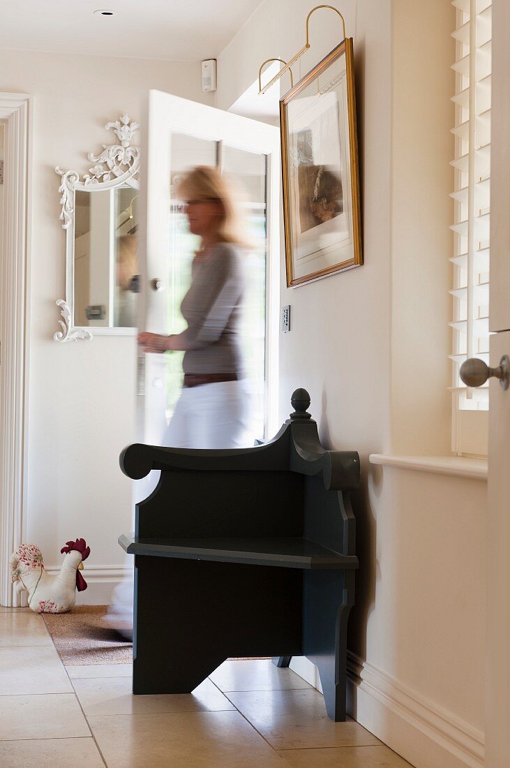 Black armchair in white hallway with woman coming in through front door