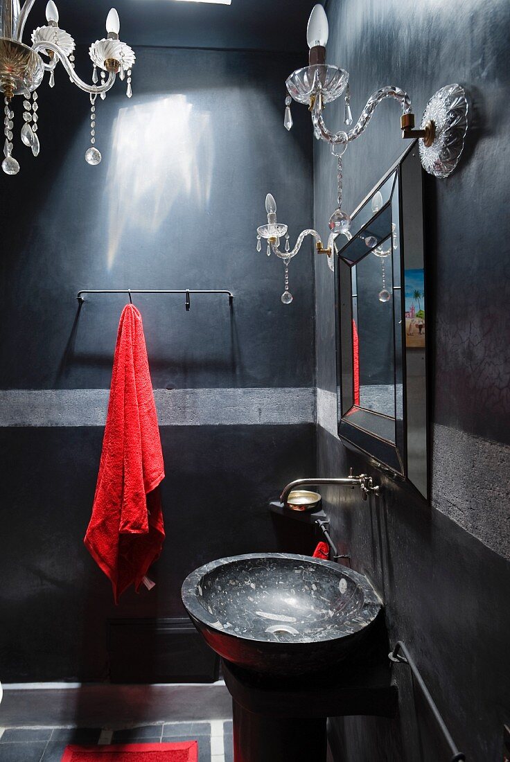 Badezimmer in Schwarz und Grau mit schwarzem Marmorwaschbecken und Kristallleuchtern; Textilien sorgen für rote Akzente