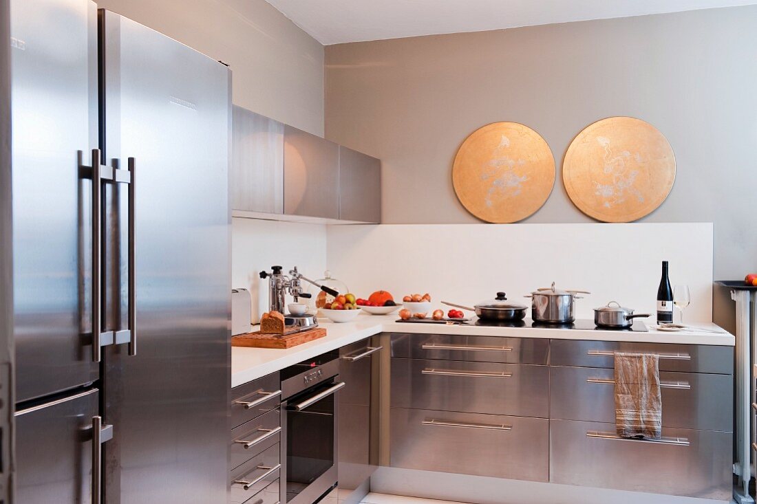 Moderne Küche mit Edelstahlfronten und weißem Spritzschutz; als Blickfang zwei goldfarbene, runde Scheiben