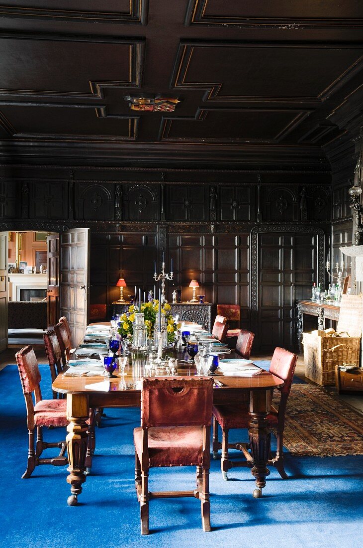 Festlich gedeckte Speisetafel in holzvertäfeltem Rittersaal mit blauem Teppich