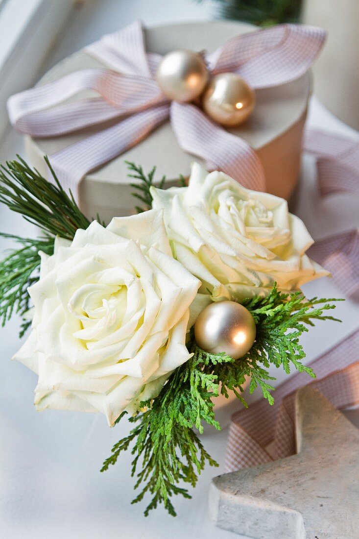 Kleiner Weihnachtstrauss aus weissen Rosen neben einer Geschenkschachtel