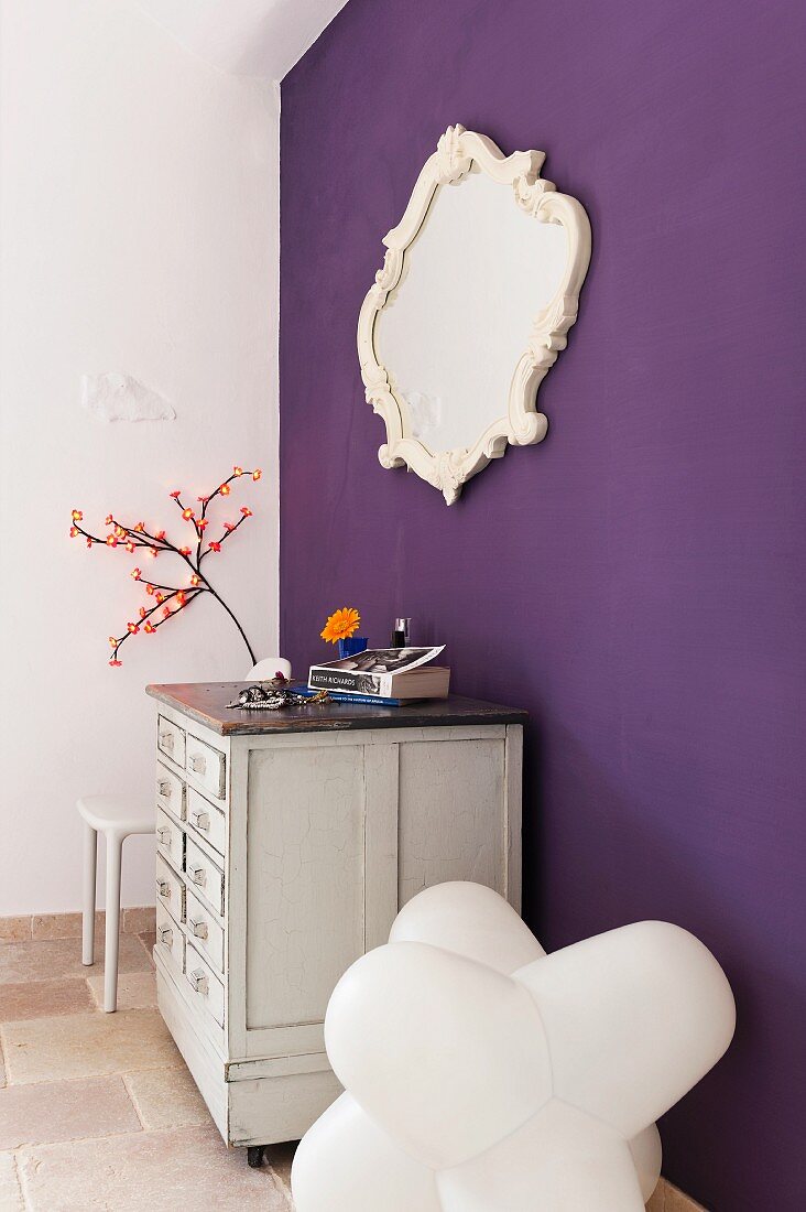 Weise Kommode, gerahmter Spiegel und Designer-Stuhl an lila Wand